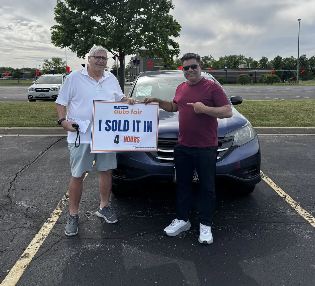 A seller and his buyer holding an I sold it in 4 hours sign in front of the car