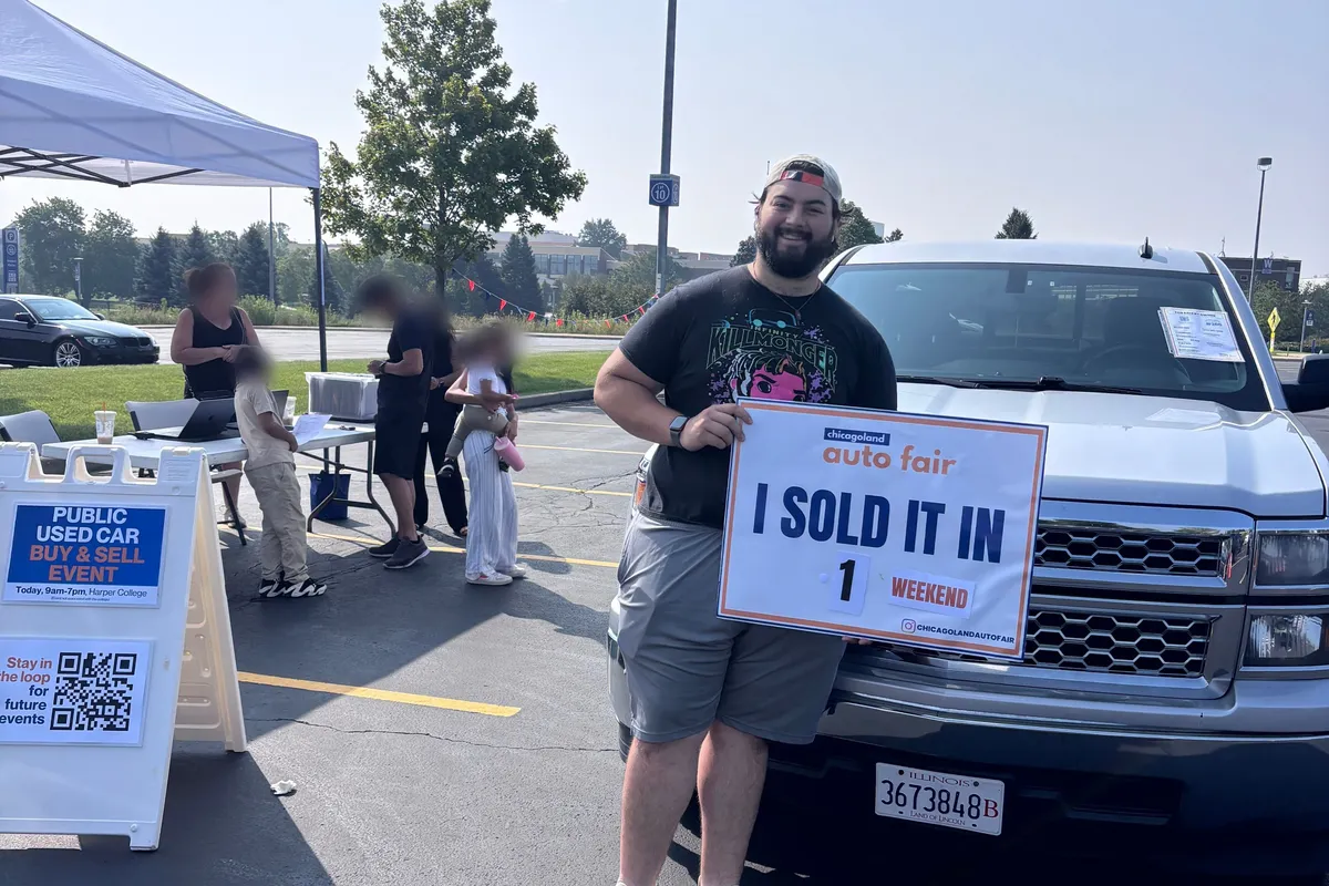 A seller holding a Chicagoland Auto Fair I sold it in 1 weekend sign beside his Chevrolet Silverado at the event check-in tent