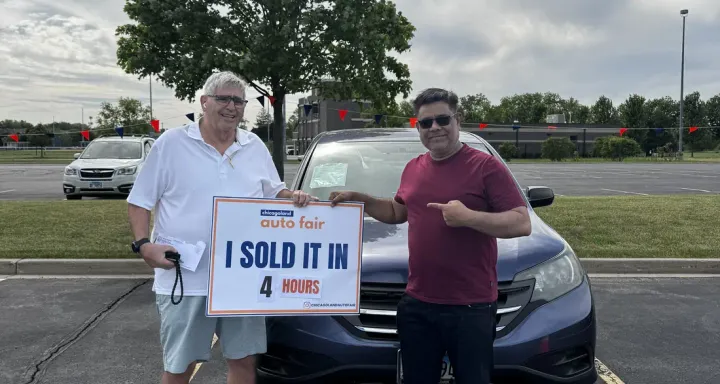 A seller and the buyer holding an I sold it in 4 hours sign in front of the car at the Auto Fair