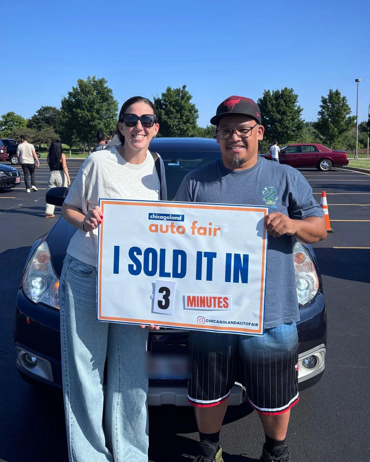 Ricardo and the buyer who bought his Subaru Outback, holding a Chicagoland Auto Fair sign that reads I sold it in 3 minutes, in front of the car on the lot.