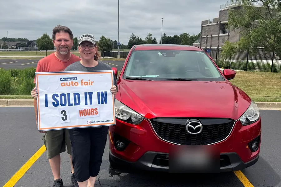 A couple holding an I sold it in 3 hours sign with their red Mazda CX-5