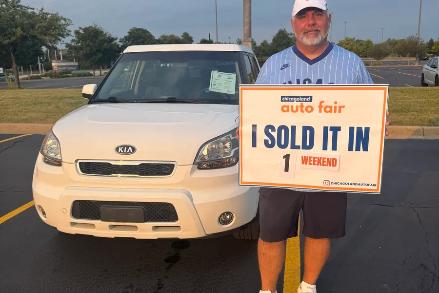 A seller holding an I sold it in 1 weekend sign with his white Kia Soul