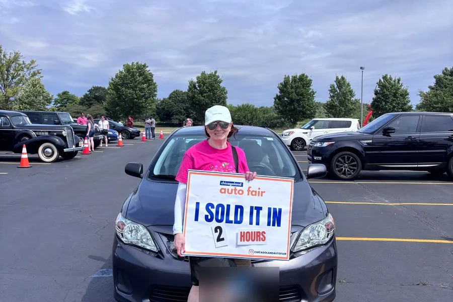 A seller holding an I sold it in 2 hours sign with her Toyota Corolla