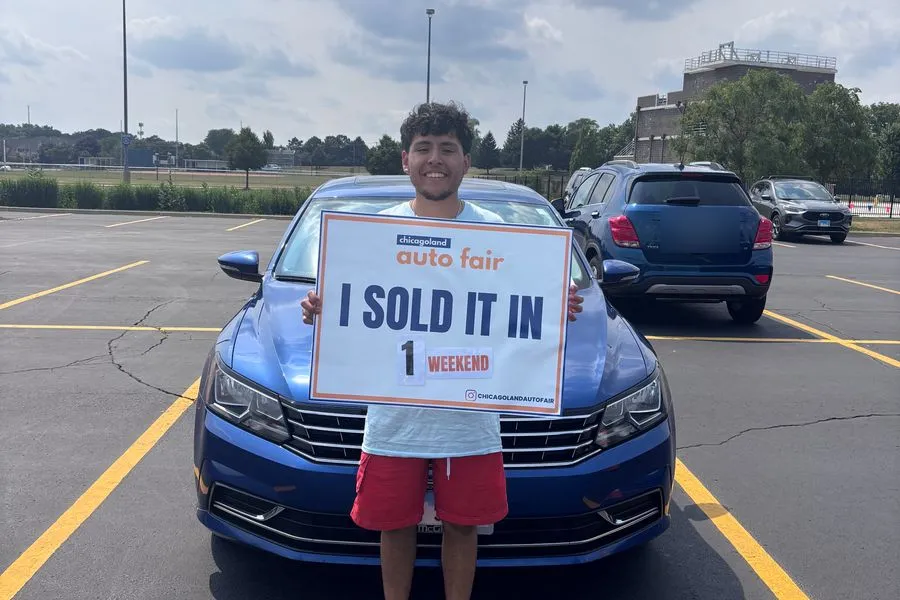 A seller holding an I sold it in 1 weekend sign with his blue Volkswagen Passat